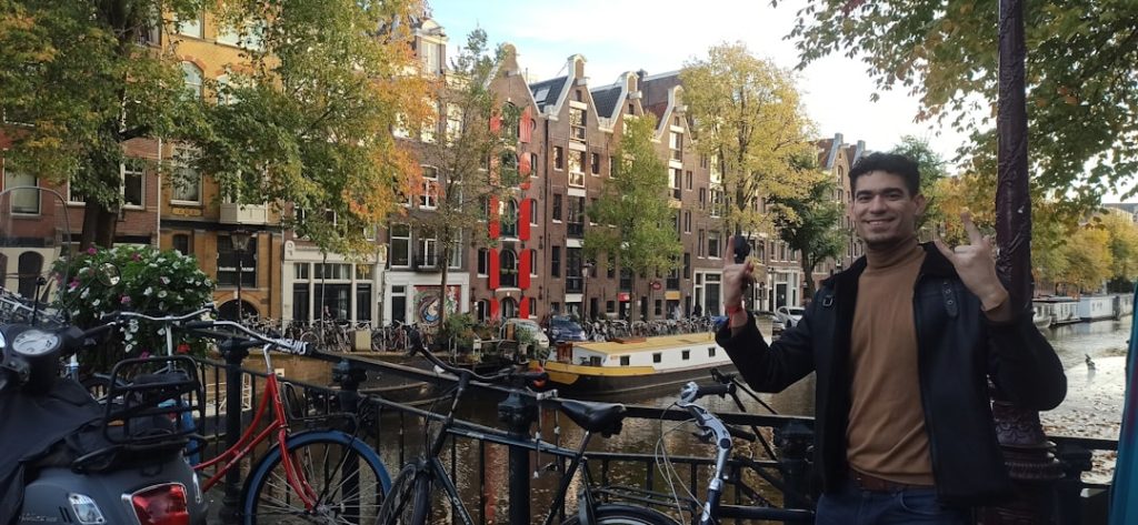 digital nomad amsterdam — a person standing next to a bike rack with a boat in the background