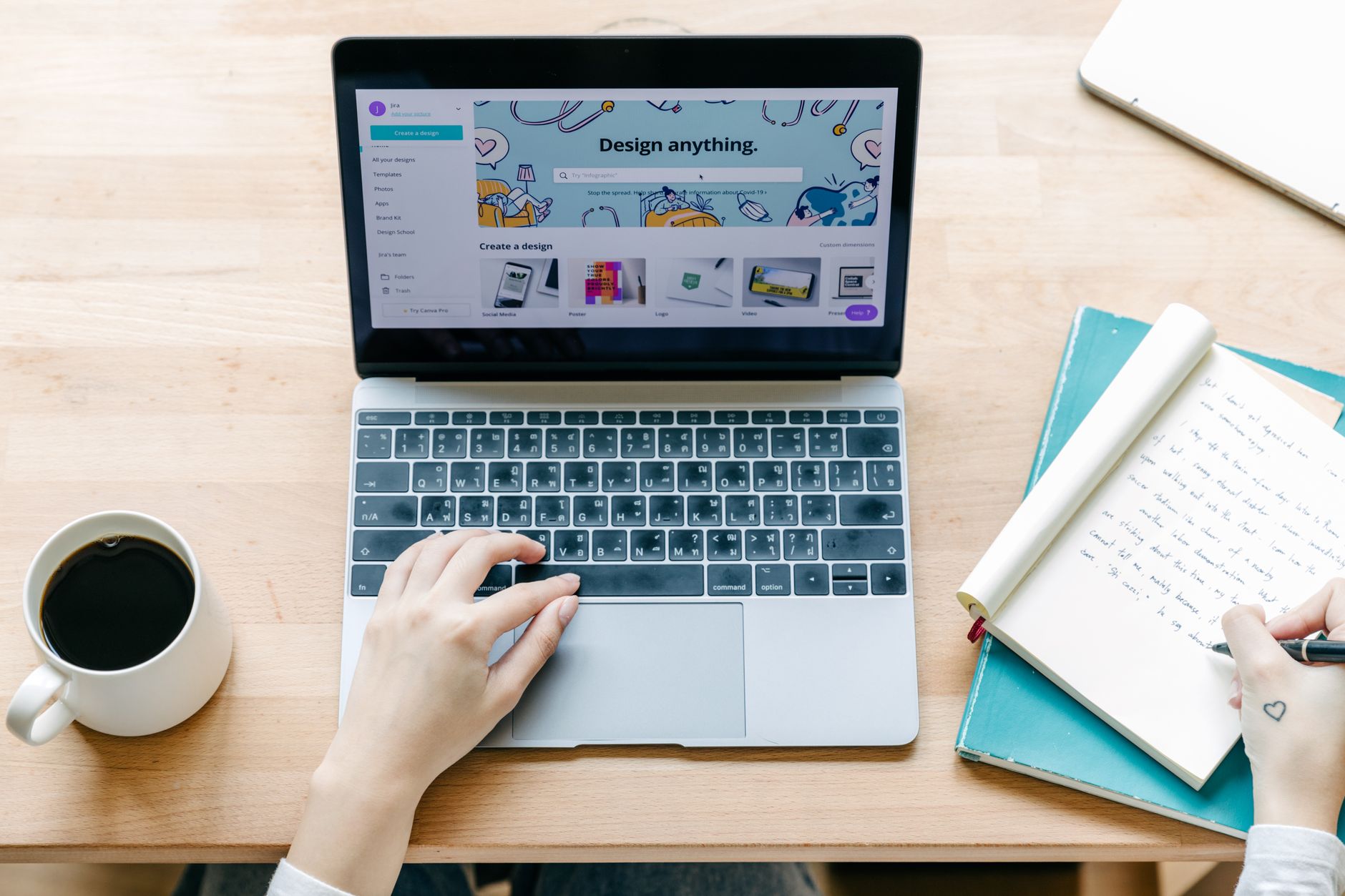 freelance tips — Unrecognizable person typing on laptop and writing notes in notebook while sitting and working on design project in modern workplace